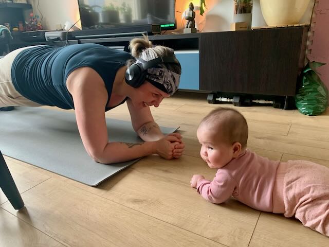 Vrouw in plank positie als onderdeel van haar postpartum herstel, terwijl haar baby voor haar ligt hetzelfde te doen op haar buik.